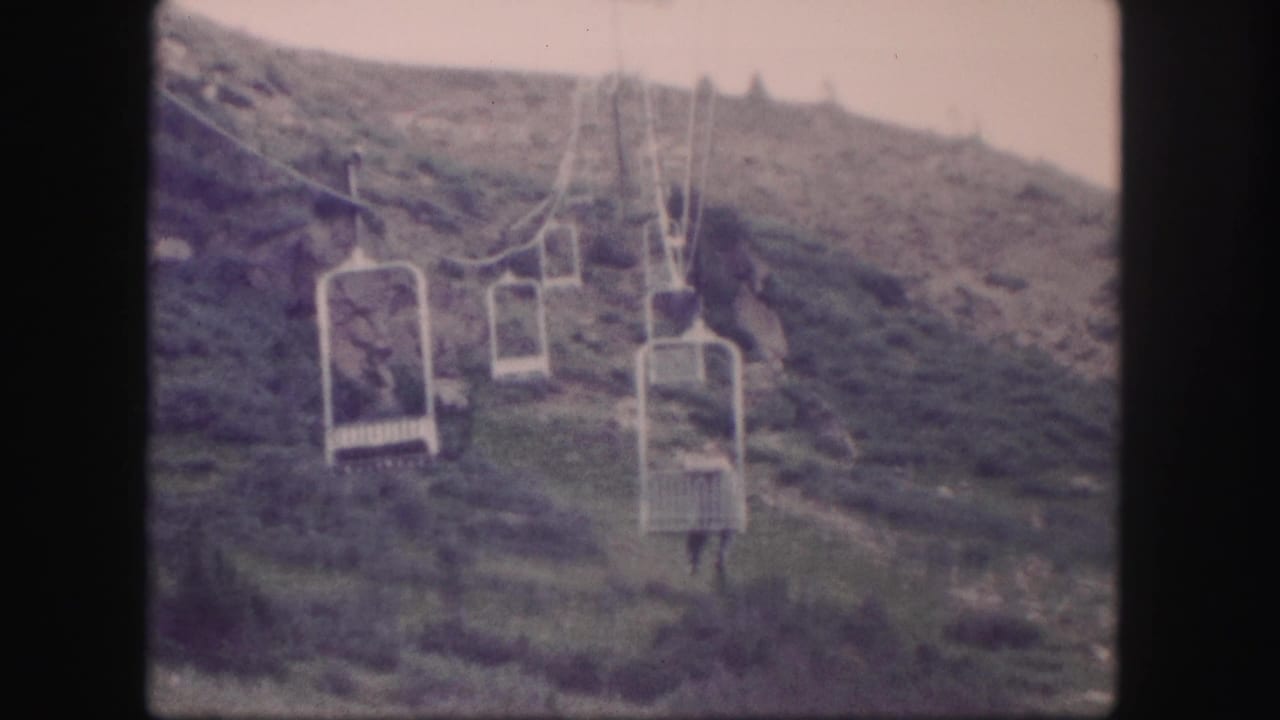 1958 Colorado 8mm frame showing empty open lift chairs on cables above a rugged mountain slope.