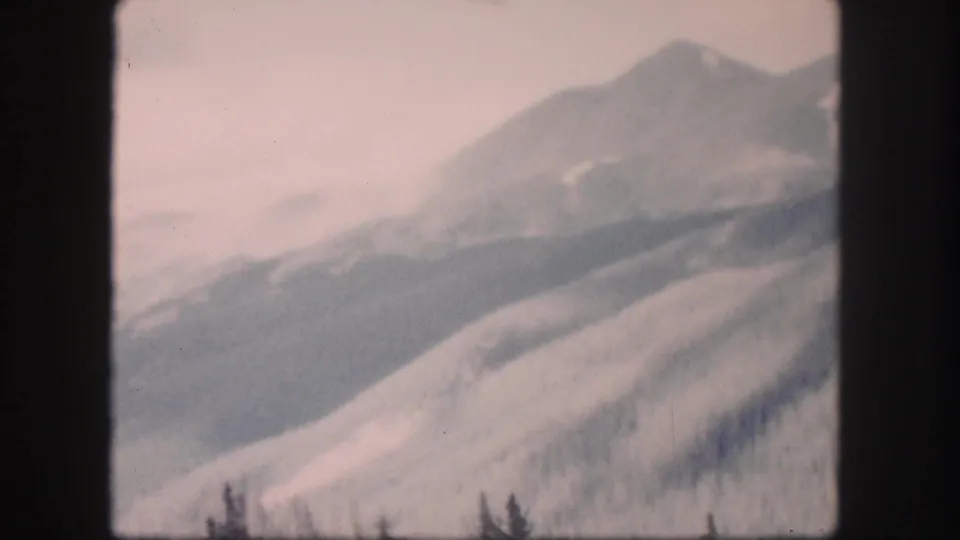 Faded 8mm view of Colorado mountain ridges and a distant peak, with no identifiable structures visible.