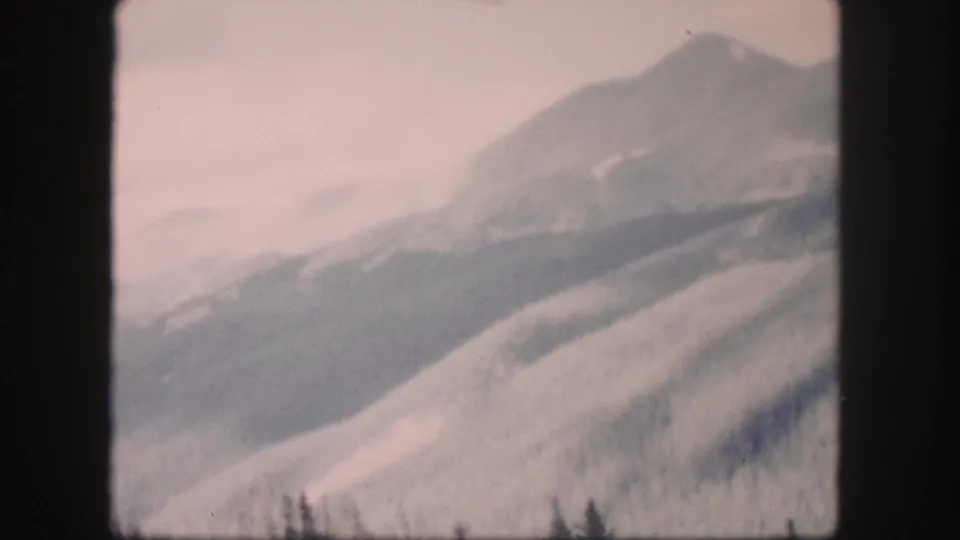 1958 Colorado home-movie frame showing a hazy mountain valley, rounded slopes, and faint trees along the lower edge.