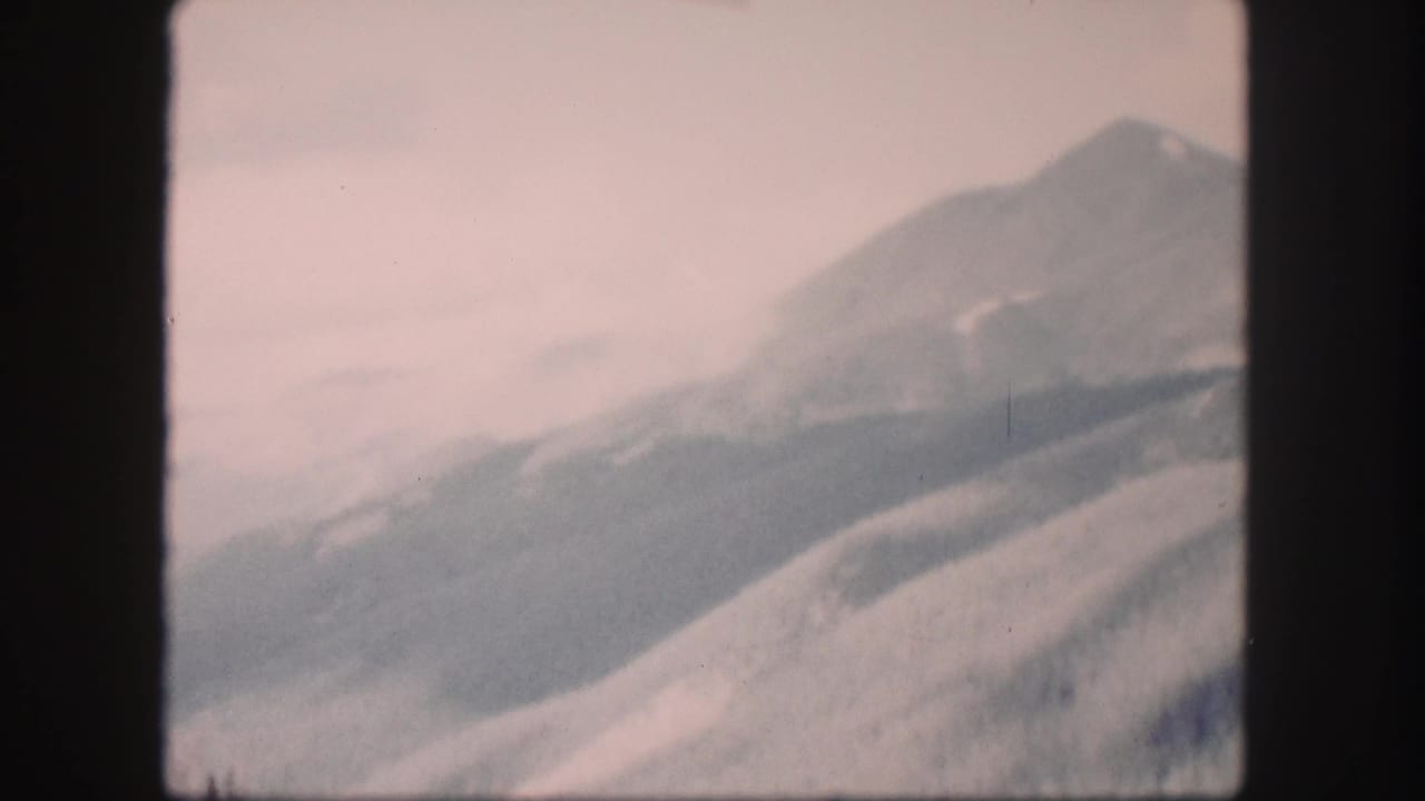 Soft mountain ridge under a pale sky, seen from a moving 8mm home movie.