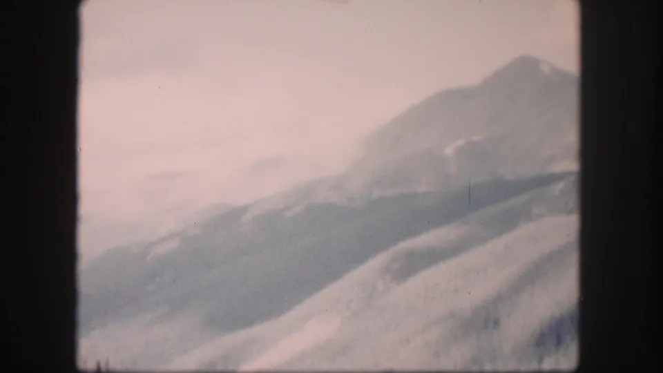 1958 Colorado 8mm frame showing a hazy mountain ridge and open slope under a washed, pale sky.
