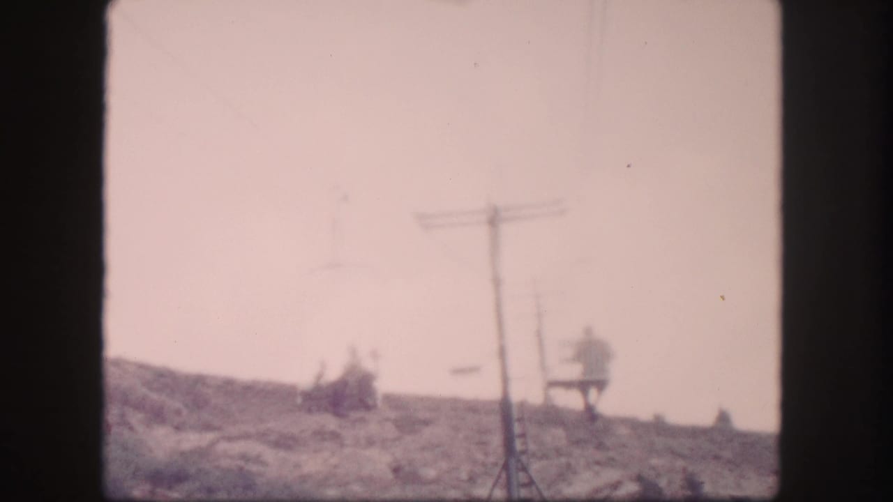 Chairlift and riders near a tall lift tower on a sloped hillside.