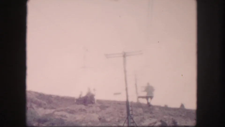 1958 Colorado home-movie frame with a chairlift crossing a sloped ski area beside a tall tower.