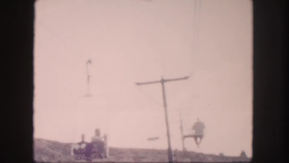 Soft 8mm frame from 1958 Colorado showing riders seated on a chairlift below a prominent tower.