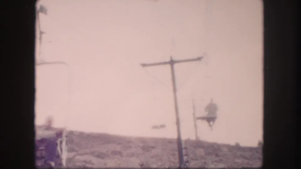 1958 Colorado 8mm frame with a chairlift rider near a support tower on a sparse mountain slope.