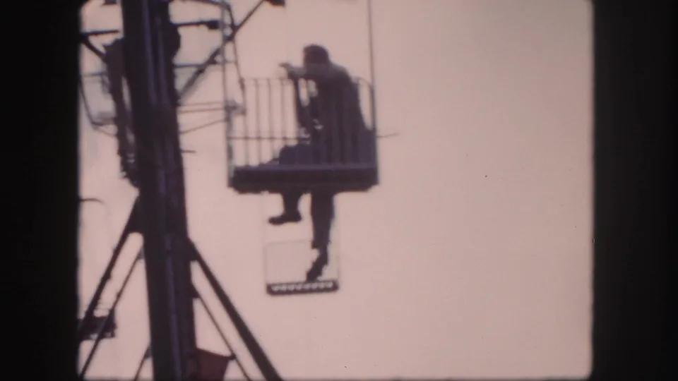 The rider remains seated in the open lift basket near the tower, with faded color and visible 8mm frame borders.