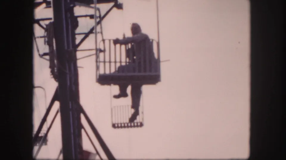 Final frame of the 1958 Colorado lift shot, with the man seated in the basket and metal tower structure visible beside him.