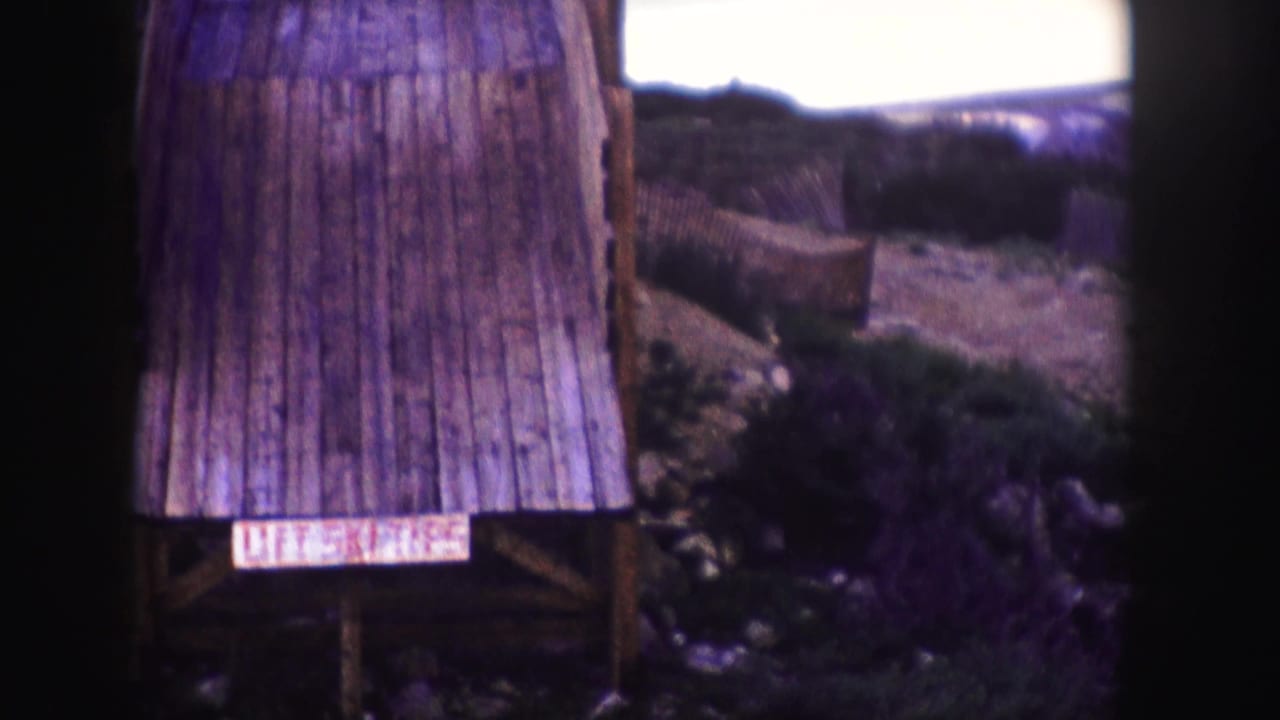 1958 Colorado home-movie frame with a close view of a rustic wooden lift-area structure and rough mountain landscape.