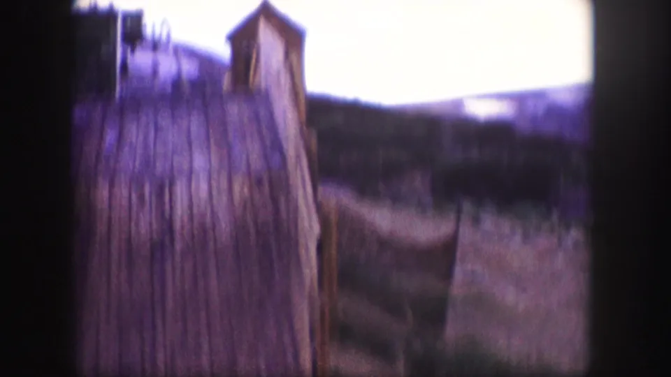 Soft 1958 Colorado 8mm frame passing near a tall rustic wooden structure with mountain terrain beyond.