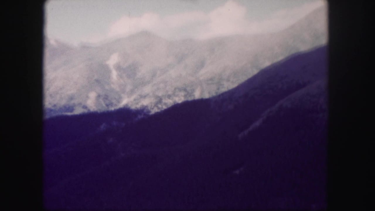 High mountain range with pale upper slopes, clouds, and dark ridge in the foreground.
