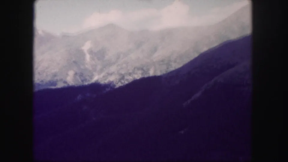 1958 Colorado 8mm view of a high mountain range partly softened by haze or cloud, with a dark foreground ridge.