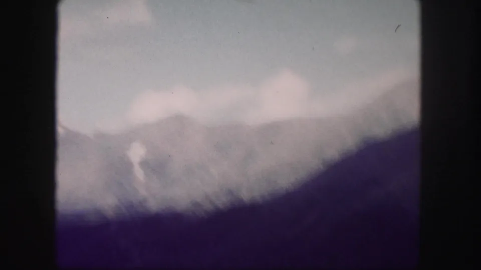 Faded 1958 Colorado 8mm frame with a soft mountain peak, pale clouds, and a dark sloped foreground ridge.