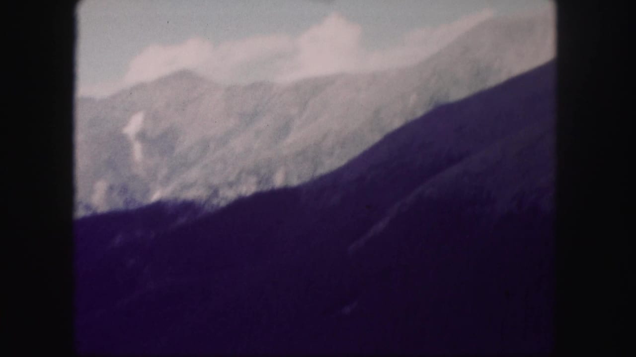 Snow-dusted mountain ridges and a dark forested slope under cloudy sky.