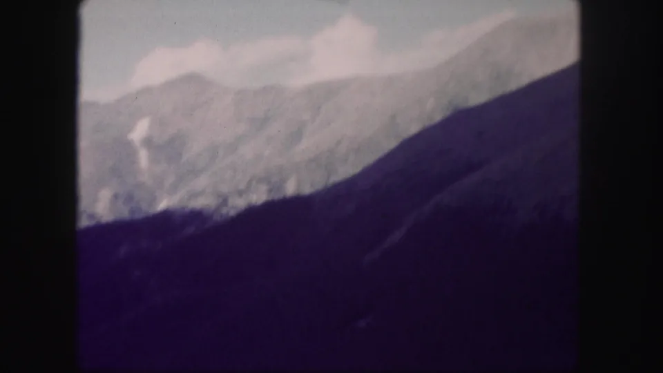 1958 Colorado 8mm frame showing distant snow-dusted ridges above a dark forested mountain slope.