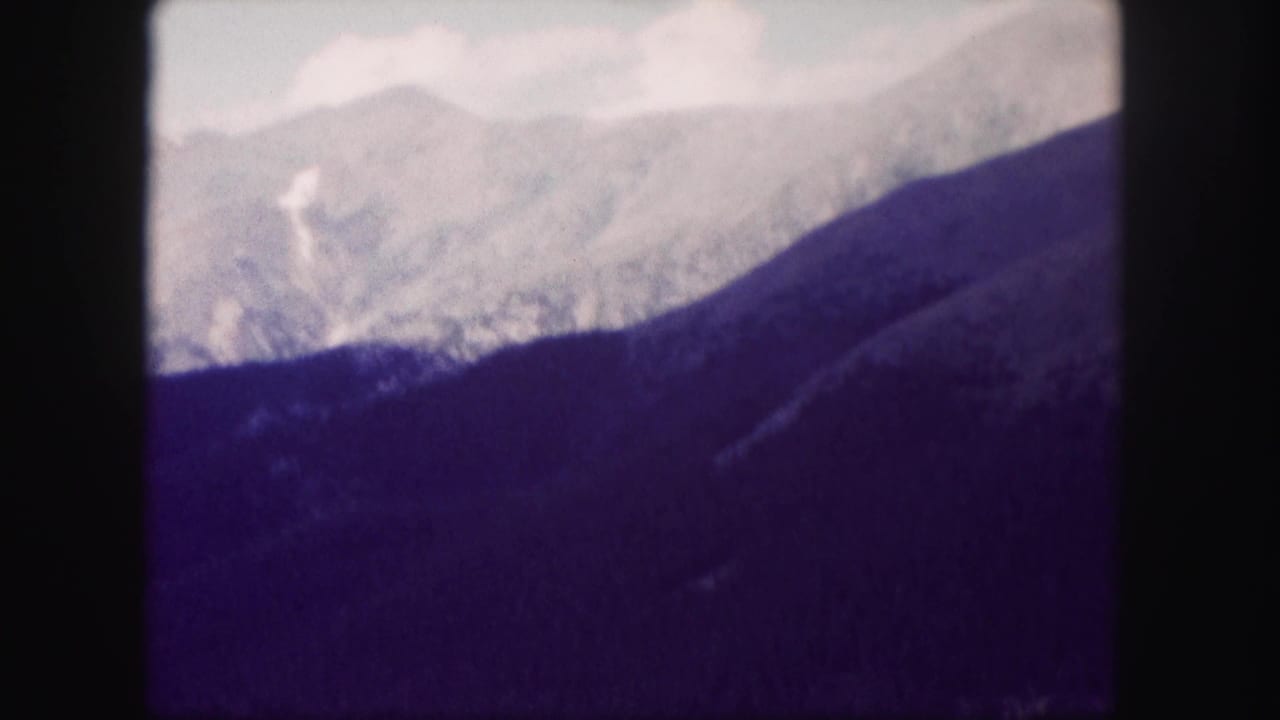 Mountain ridges seen above a dark wooded slope with soft focus and cloudy sky.