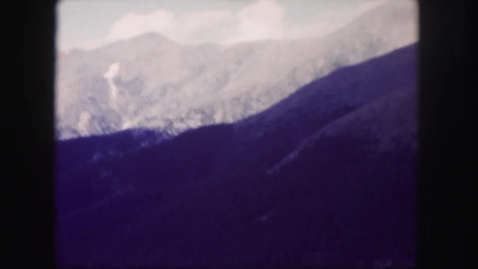 Colorado mountain landscape in soft 8mm color, with pale ridges above a dark wooded slope.