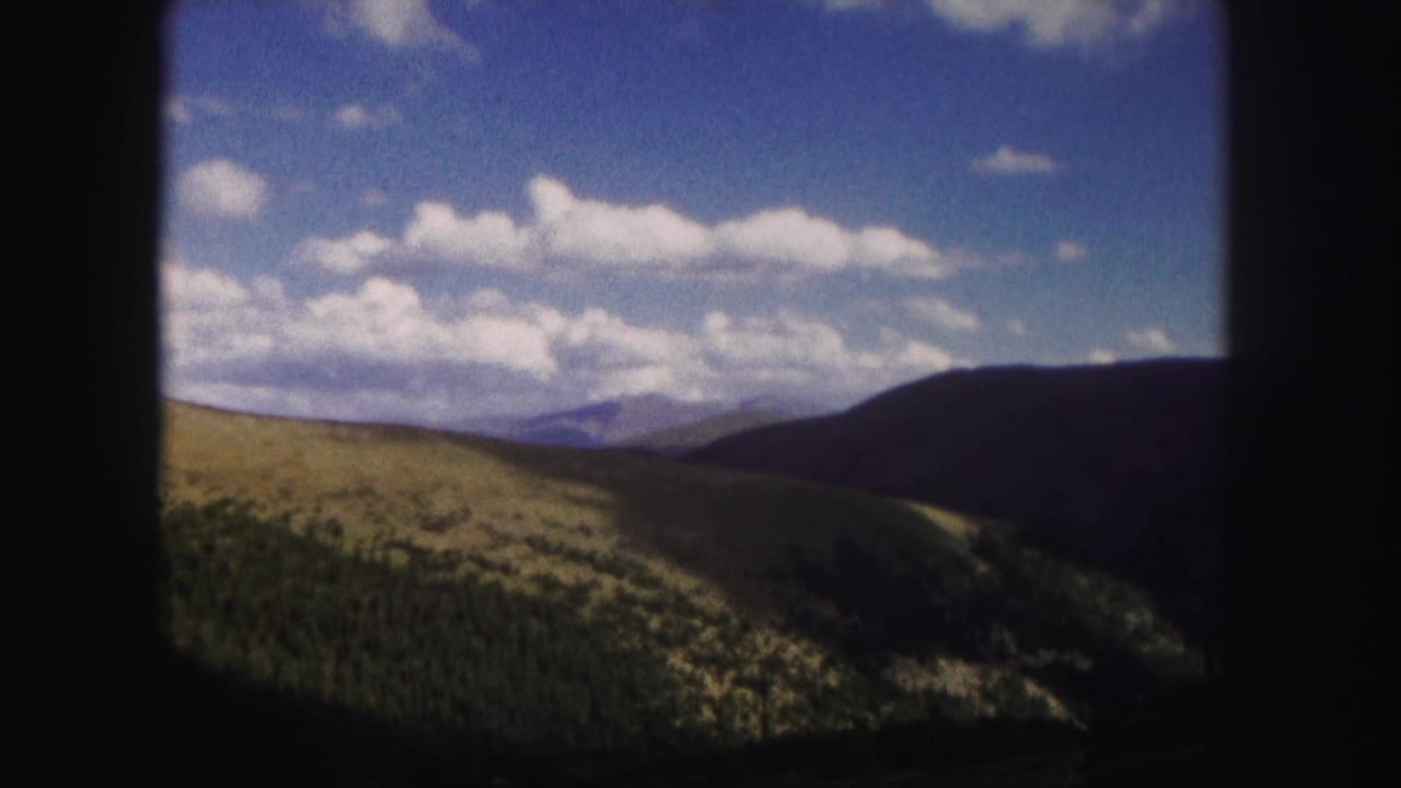 Mountain panorama with sunlit hills, dark ridge, and clouds across a blue sky.