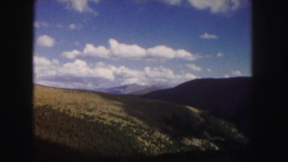 1958 Colorado 8mm still showing layered hills, a distant mountain line, bright clouds, and heavy dark film-frame borders.