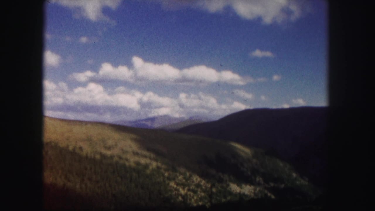 Mountain valley with green slopes, dark ridge, blue sky, and clouds.