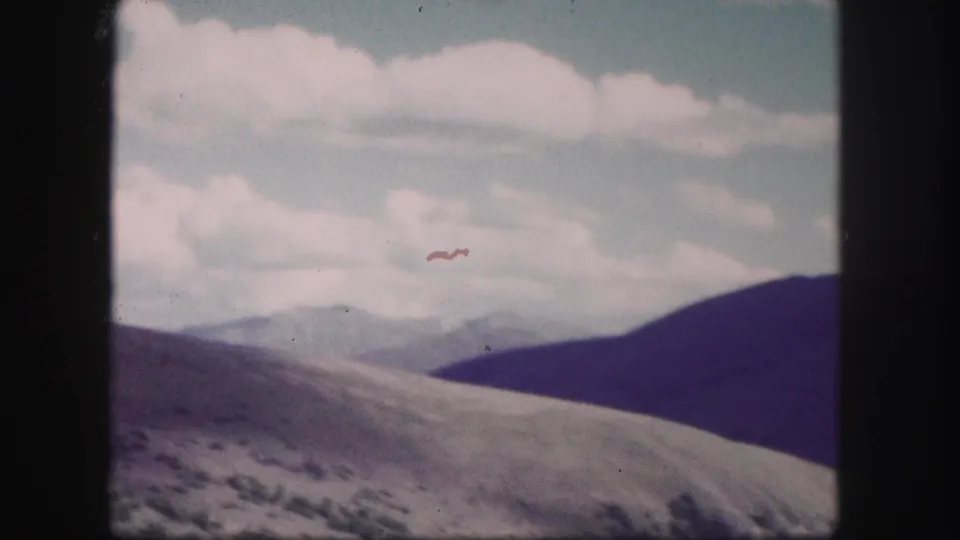 1958 Colorado 8mm frame showing rolling hills, shadowed mountain slopes, distant ridges, and pale clouds with visible film wear.