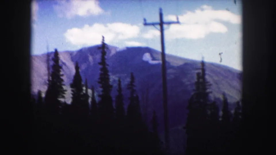 1958 Colorado 8mm frame showing evergreen silhouettes, distant mountains, scattered clouds, and a roadside utility pole.