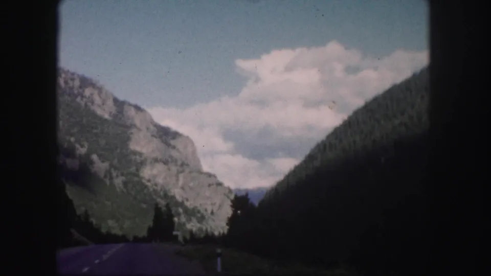 The Colorado road view continues through a mountain valley, framed by 8mm film borders and soft faded color.