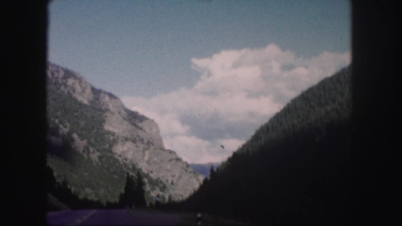 Rocky mountain pass with dark forested slope and clouds above the roadway.