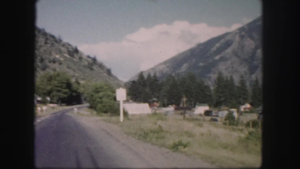 1958 Colorado 8mm view of a curving highway passing a roadside sign and small buildings in a mountain valley.