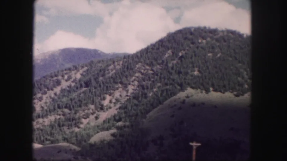 Colorado mountain view on 8mm film with wooded slopes, bright clouds, and a utility pole near the lower right edge.