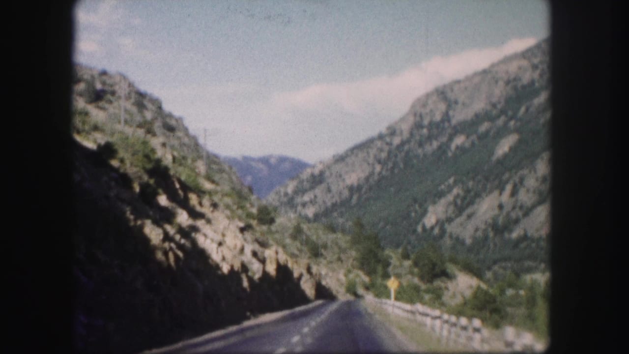 Paved road running through a rocky mountain canyon with guardrail.