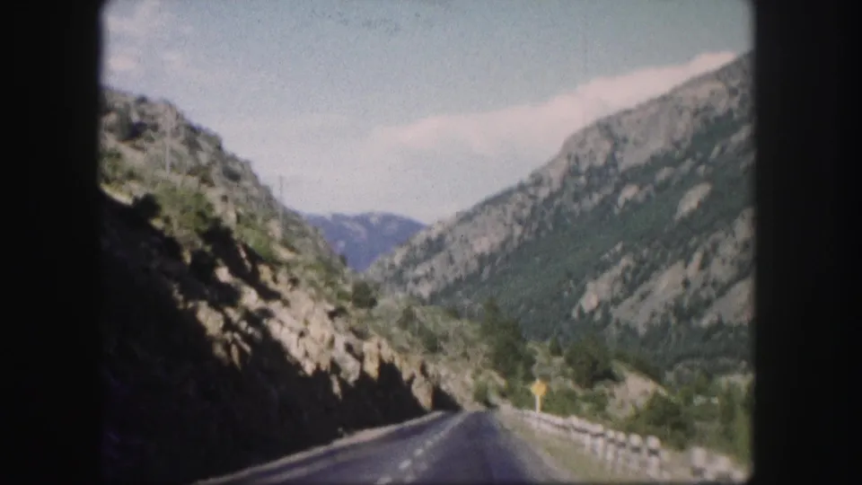 1958 Colorado 8mm road view through rocky canyon walls, with a guardrail and distant mountains ahead.