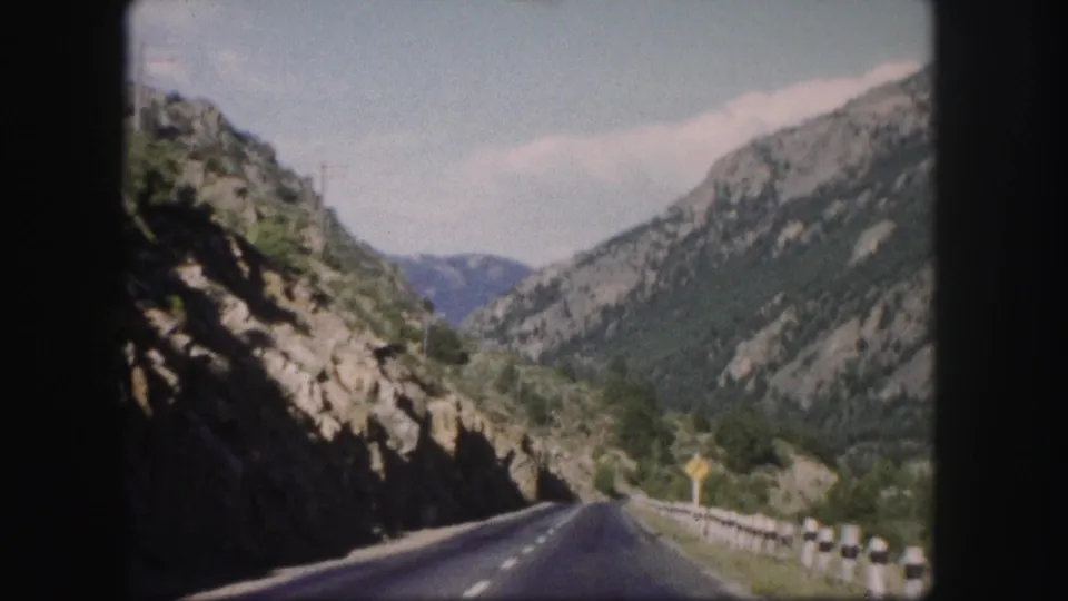 1958 Colorado 8mm frame from a moving road trip, looking ahead along a mountain highway between rocky slopes.