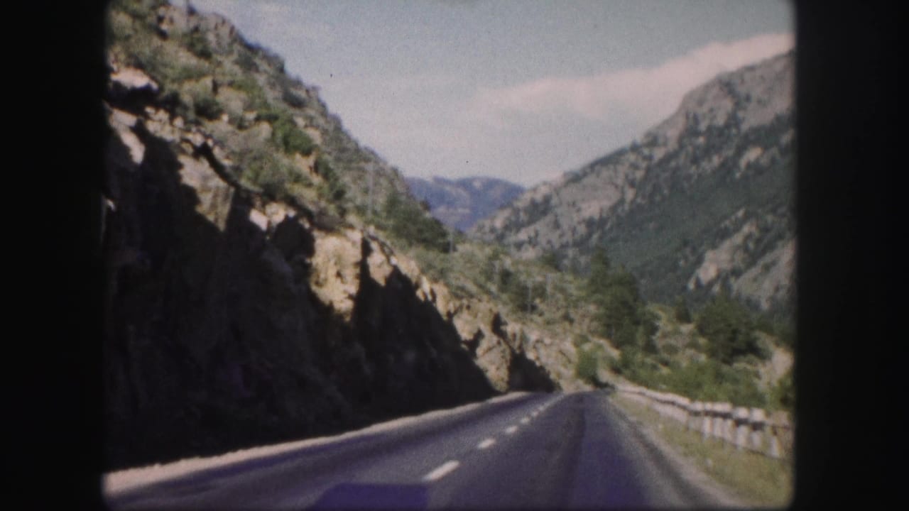Mountain highway curves along a rocky cliff with guardrail and distant ridges.