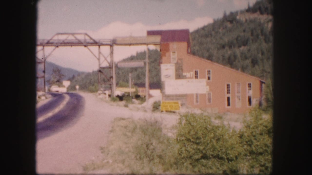 Curving mountain road beside a red brick industrial building and metal overhead structure.