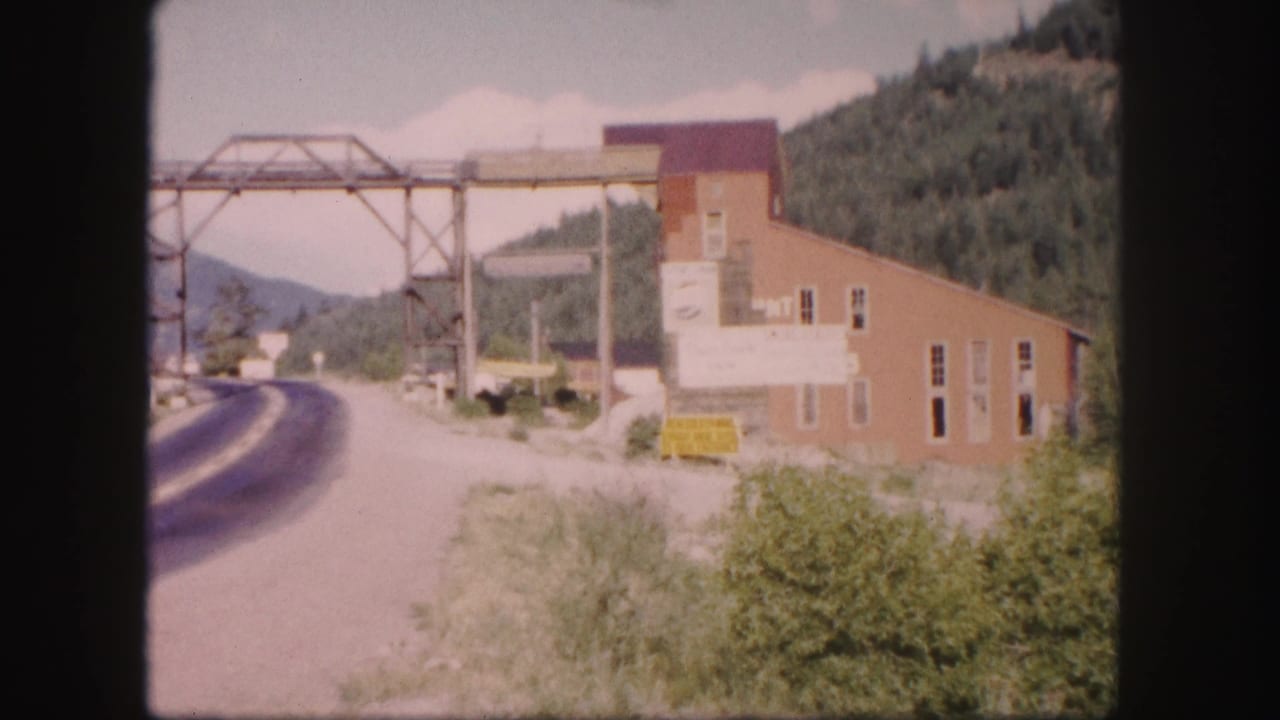Roadside brick building with a metal gantry above the road and wooded hills behind.