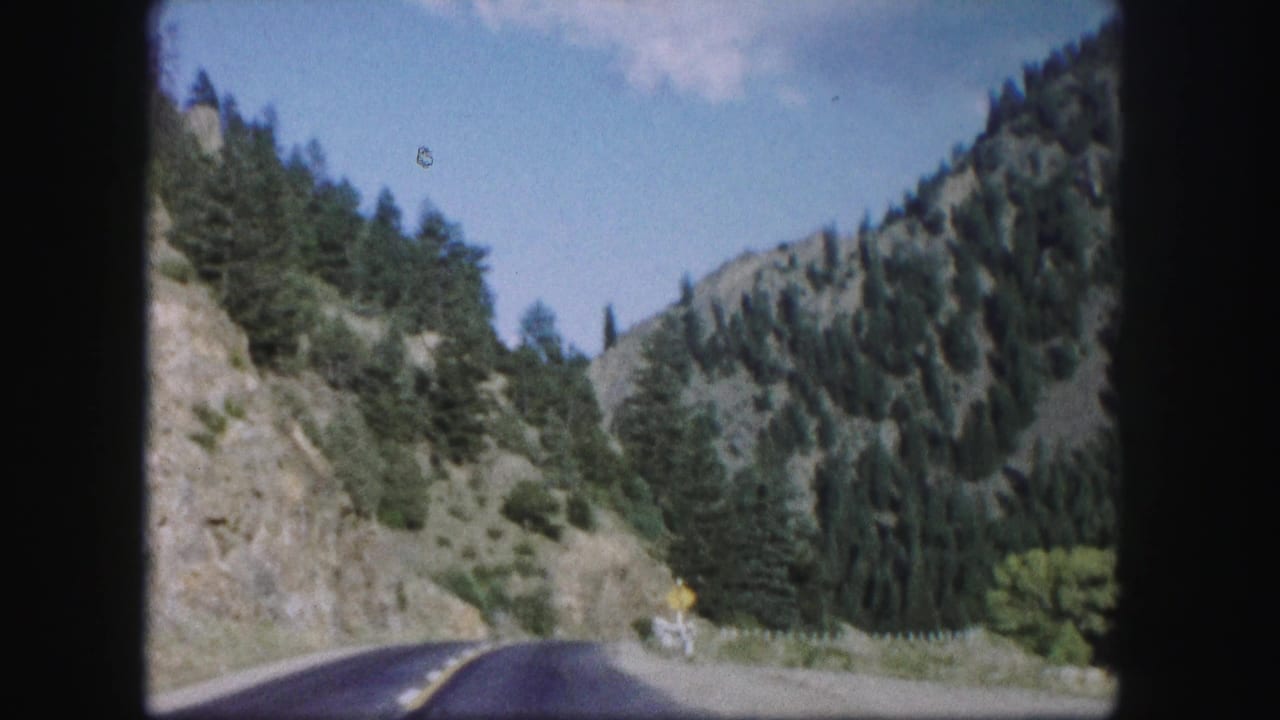 Paved road curving through a steep, forested mountain valley.