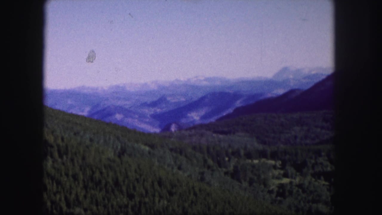 Green hillside descending toward a hazy mountain valley with blue ridges beyond.