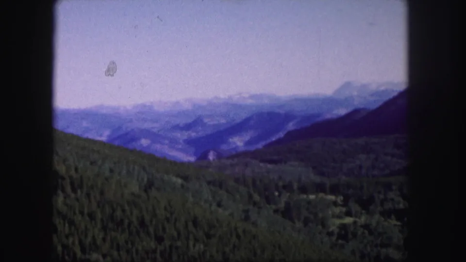 1958 Colorado home-movie still with evergreen slopes, layered mountain ridges, and atmospheric haze across the valley.