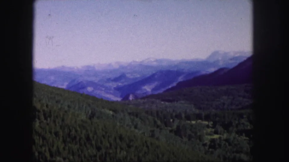 Colorado 1958 8mm still showing soft-focus forested slopes, blue-purple mountain layers, and a hazy distant valley.