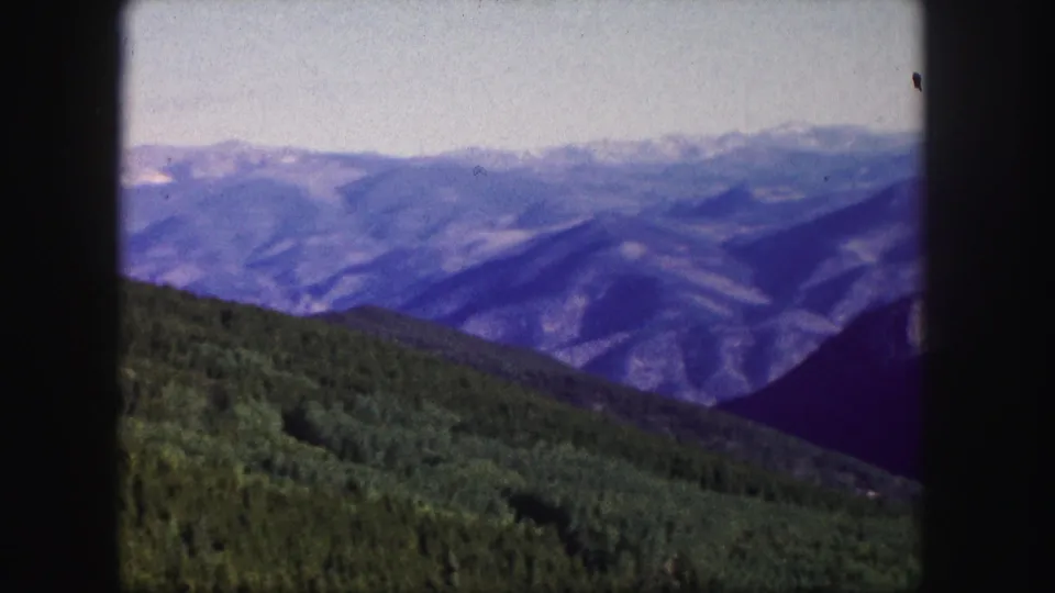 Colorado 1958 8mm still showing rolling green hills in front of blue-purple mountain ridges and a bright sky.