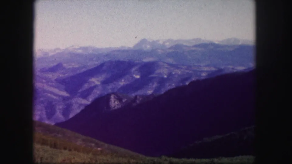 1958 Colorado home-movie frame with soft-focus mountain layers, shadowed slopes, and a low foreground ridge.