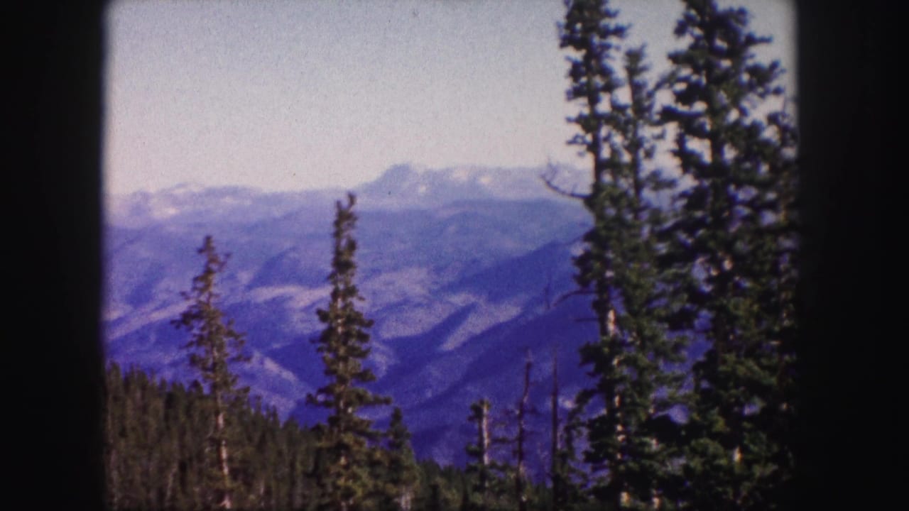 1958 Colorado 8mm frame showing evergreen trees in the foreground and layered mountain ridges in the distance.