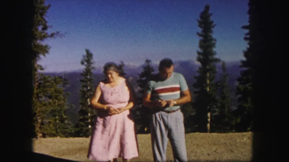 At a Colorado mountain overlook, a woman in a pink dress and a man in a striped blue shirt look down at something in their hands.