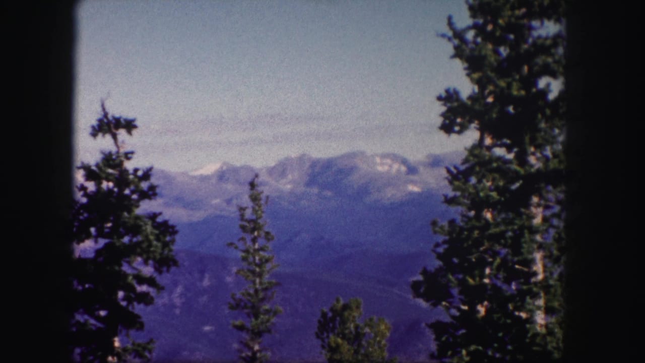 Distant mountain ridge seen through conifer trees with dark film borders.