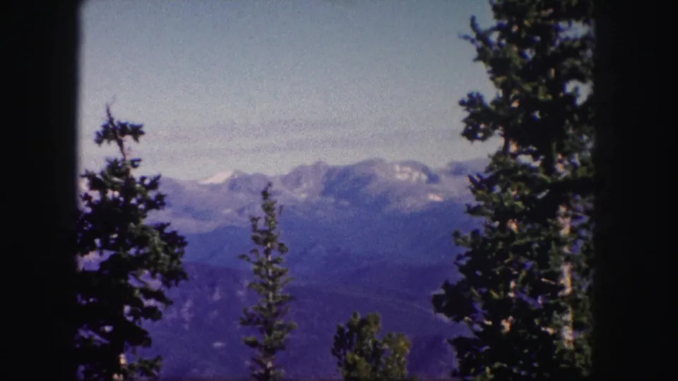 1958 Colorado 8mm view of a blue-purple mountain ridge framed by conifers and soft dark edges from the film scan.