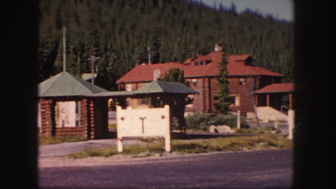 1958 Colorado 8mm frame showing a rustic log lodge with red roof, white tourist sign, small log structures, and pine-covered hillside.