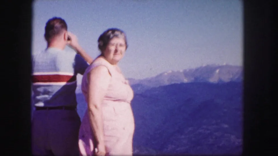 Woman in a pink dress faces the camera at a Colorado mountain overlook while a man looks away.