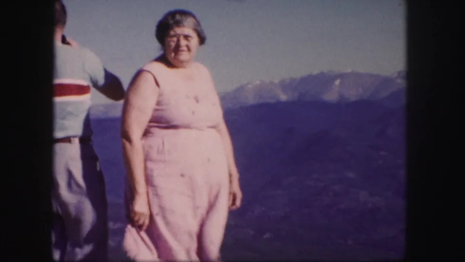 Woman in a pink dress stands at a Colorado mountain overlook with a man partly visible beside her.