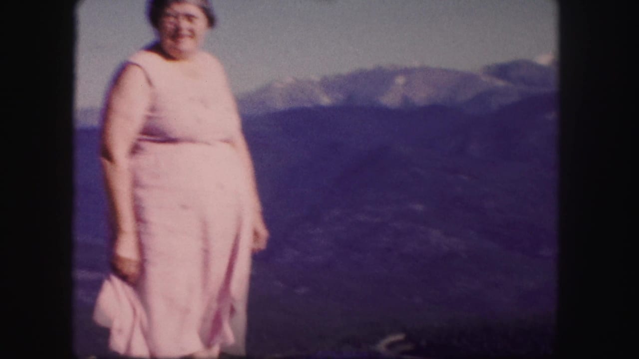 Woman in a pink dress standing before distant mountains.