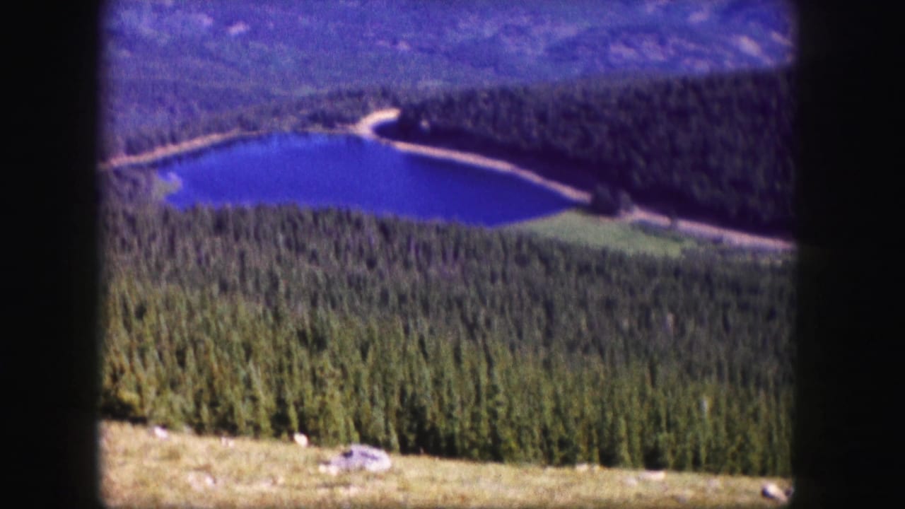 High view of blue lake, forested slopes, shoreline track, and dark film borders.